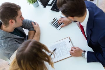Couple consulting with a financial advisor, reviewing documents and using a calculator