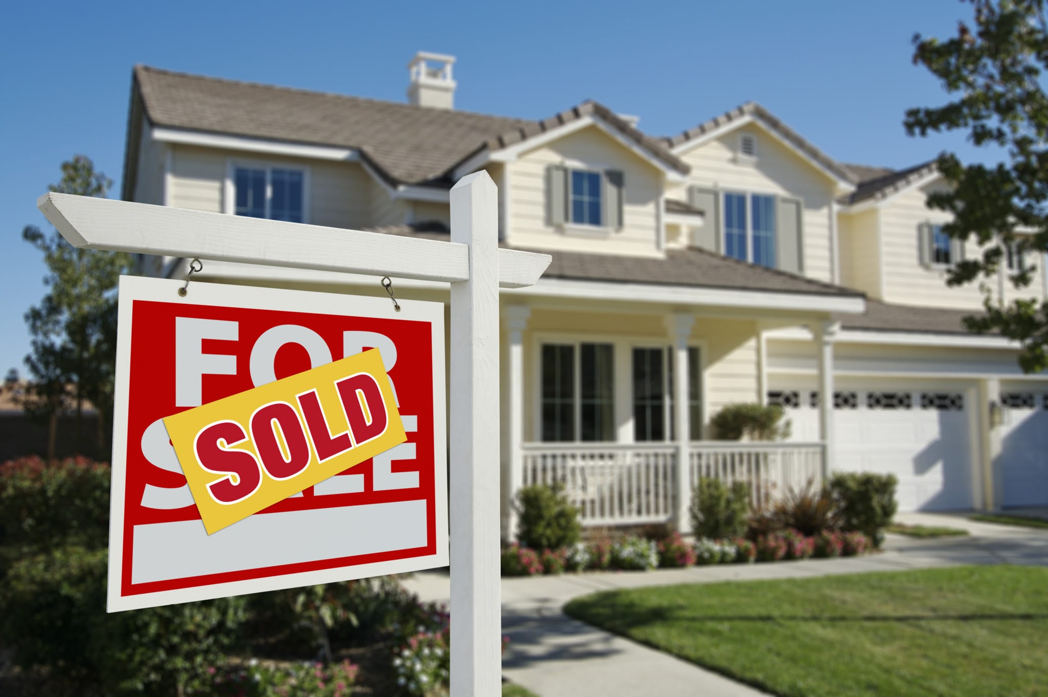 Sold sign in front of a suburban house with a manicured lawn and front porch.