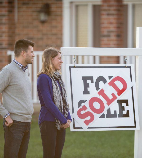 Couple standing next to sold sign