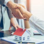 mortgage lender and homeowner shakes hand, and one wooden house on table