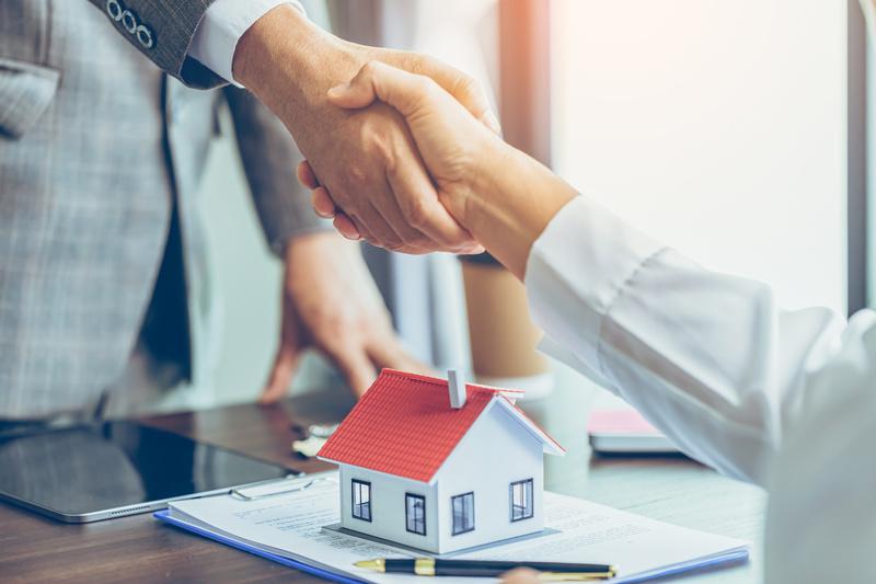 mortgage lender and homeowner shakes hand, and one wooden house on table