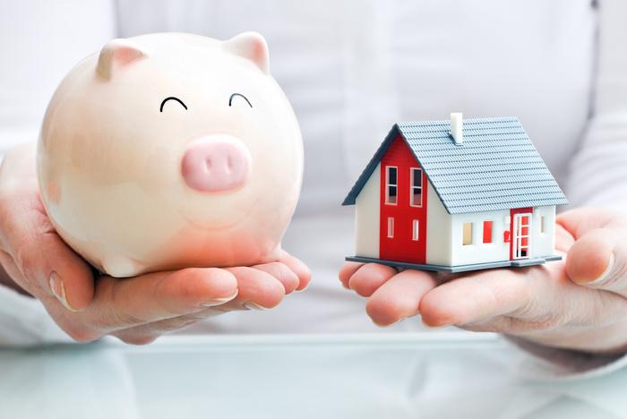 Hands holding a piggy bank and a house model - home financing concept