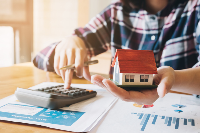 woman calculating budget before signing real estate project contract with house model at the table in the home- Home Purchase vs Refinance concept