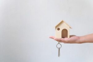 Hand holding wooden house and home keychain. Property investment and house financing