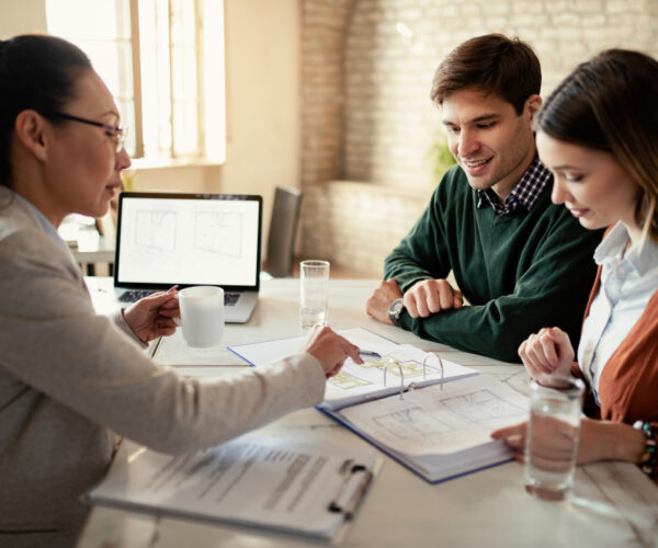 Smiling couple and insurance agent going through real estate plans during a meeting in the office. Focus is on man.