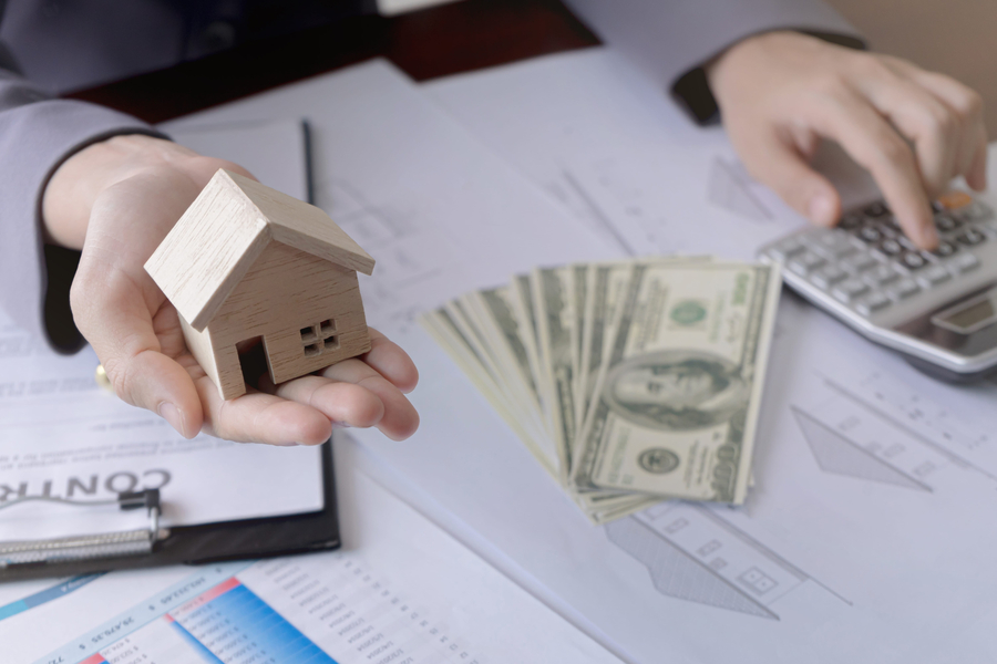 Real estate agent showing a miniature model house to the customer and using calculator. Concept for real estate investment and loan.